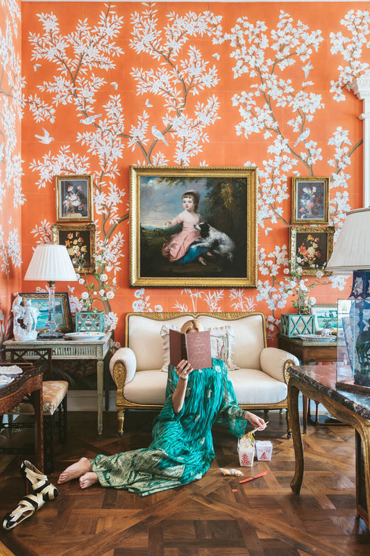 red floral wallpaper with young woman reading a book eating food.