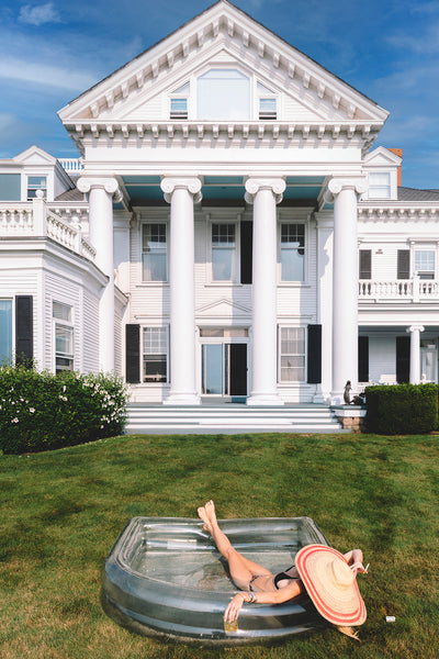 Large white house with inflatble pool and woman in bikini relaxing 