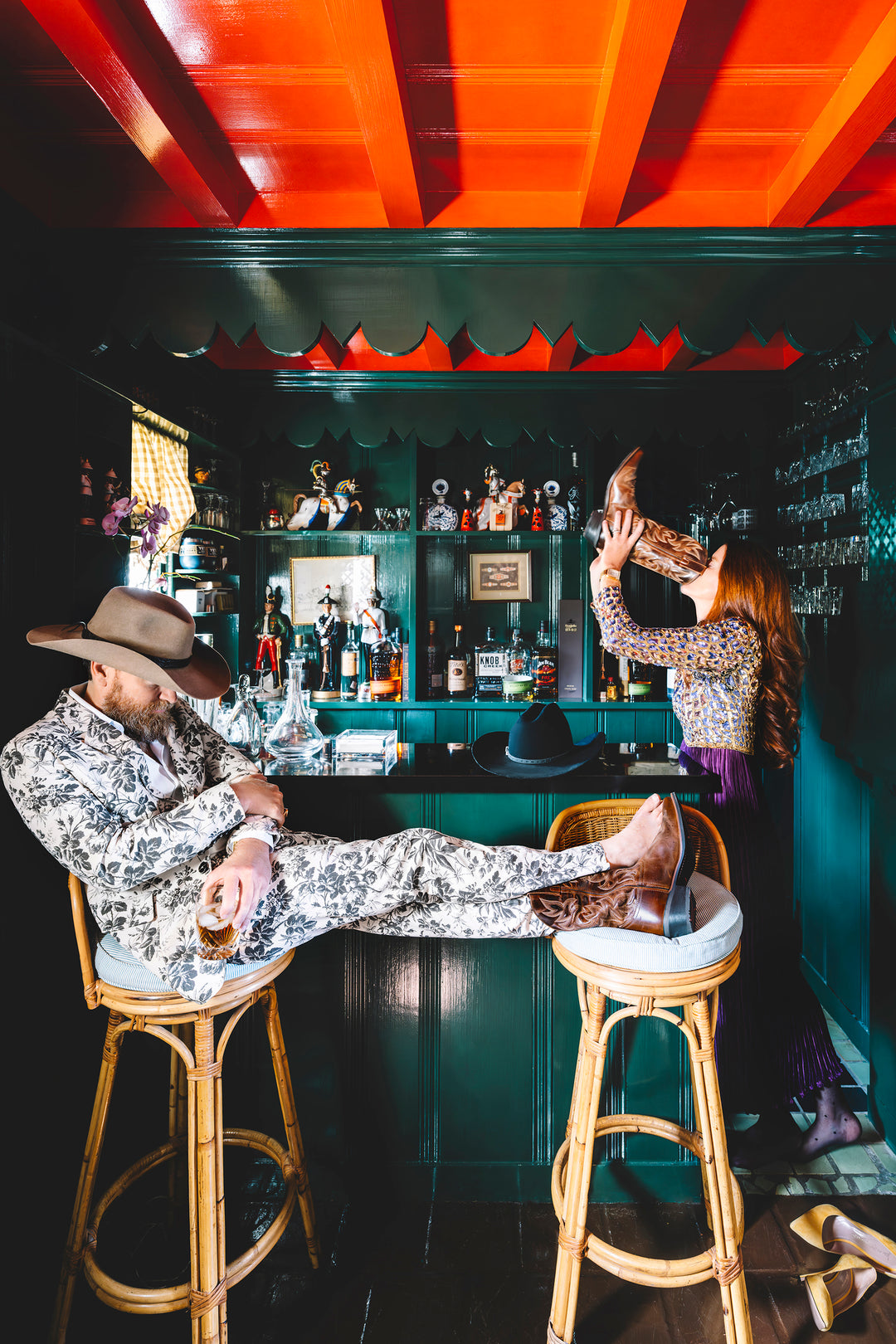 Man and woman at a bar. woman in purple dress drinking from the man's boot while the gentleman sleeps in a barstool.