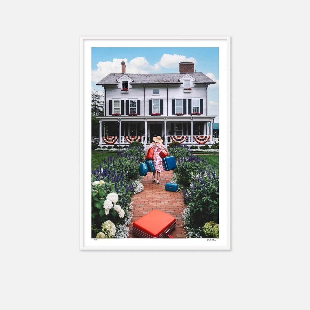 Nick Mele Fine Art Print, titled Checking In - Woman with suitcases walking towards a large white house with a garden.