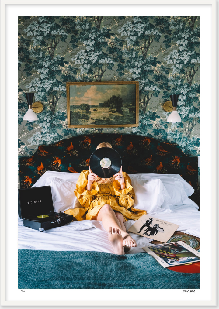 framed images of girl in yellow dress laying on bed with green leaf wallpaper surrounded by a vintage record player and records. 