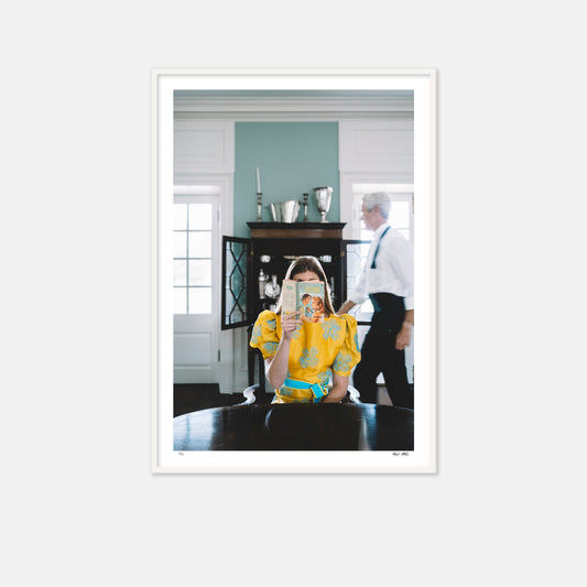 Framed photograph of a woman in a yellow dress holding a mirror, with a man in a white shirt in the background.