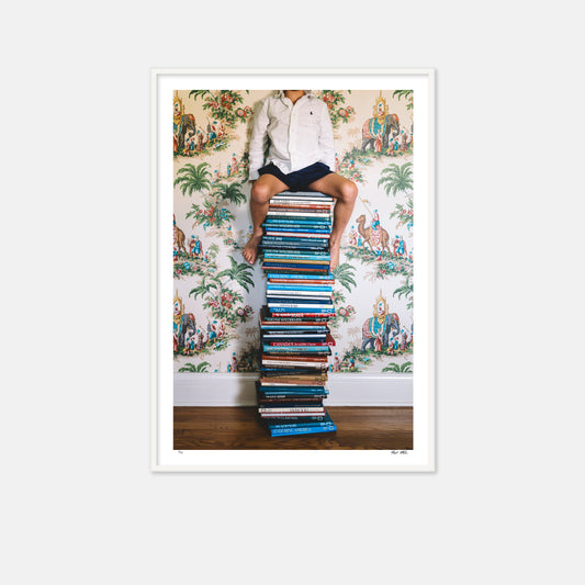 young boy sitting on stacked books with a  backdrop of camel wallpaper