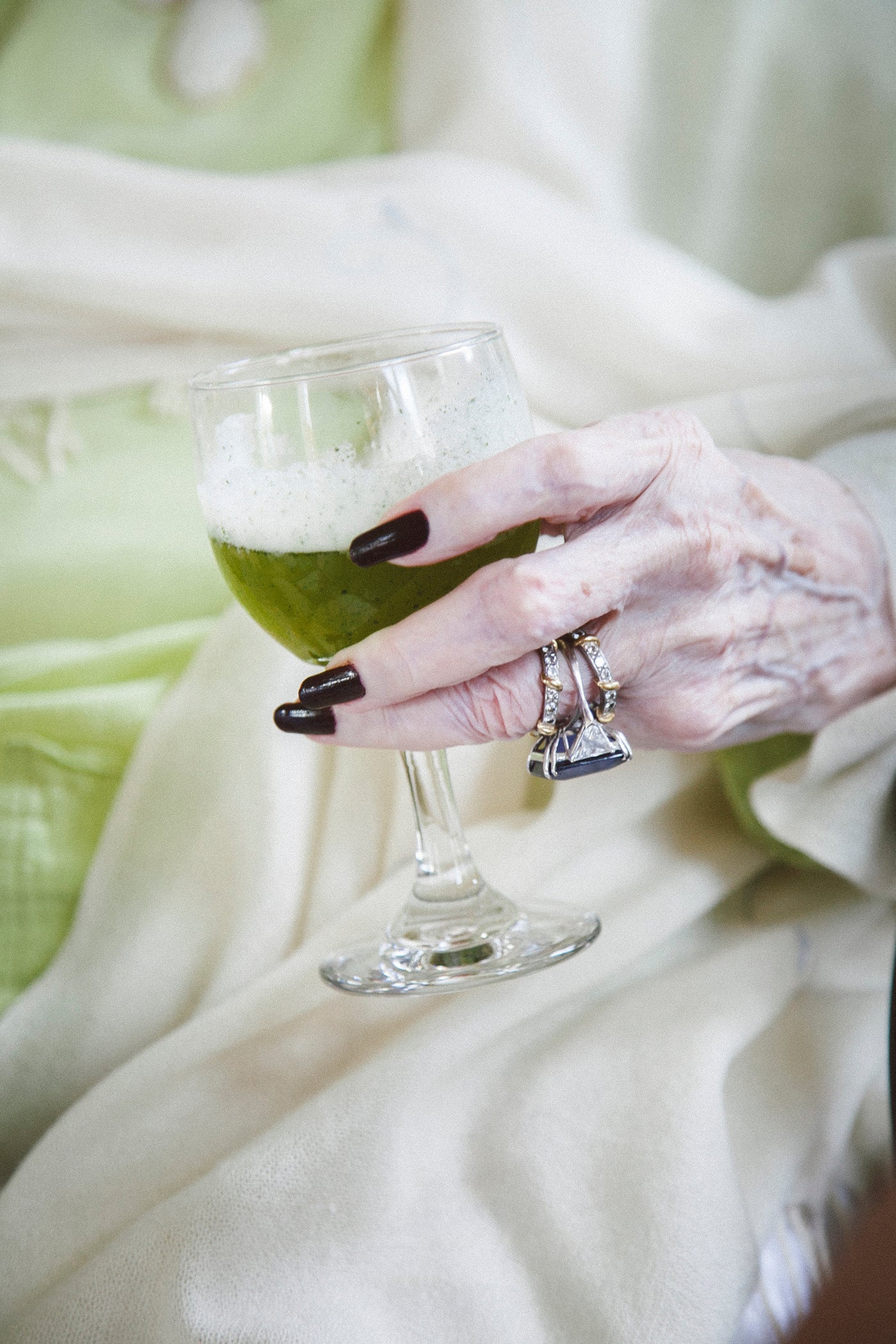 Grand dame hands with green cocktail juice. dramatic jewelry and lime green dress