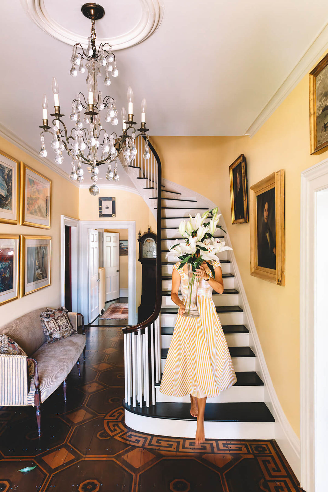 A women in a fashionable dress at the bottom of a grand staircase with a big flower arrangement covering her face