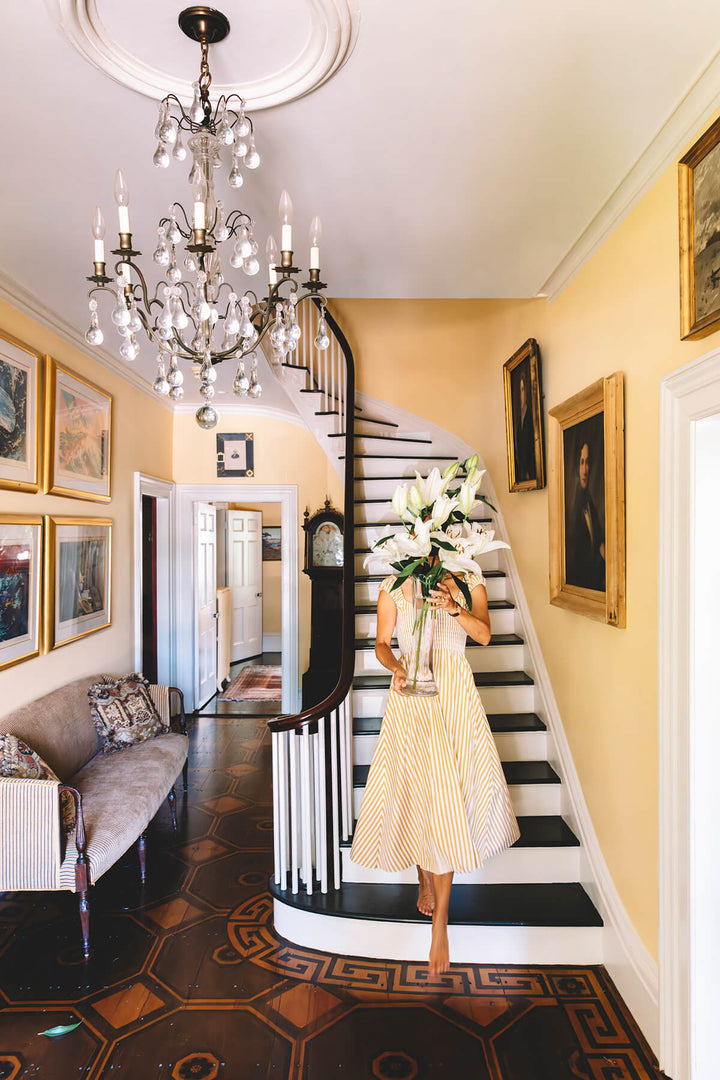 A women in a fashionable dress at the bottom of a grand staircase with a big flower arrangement covering her face