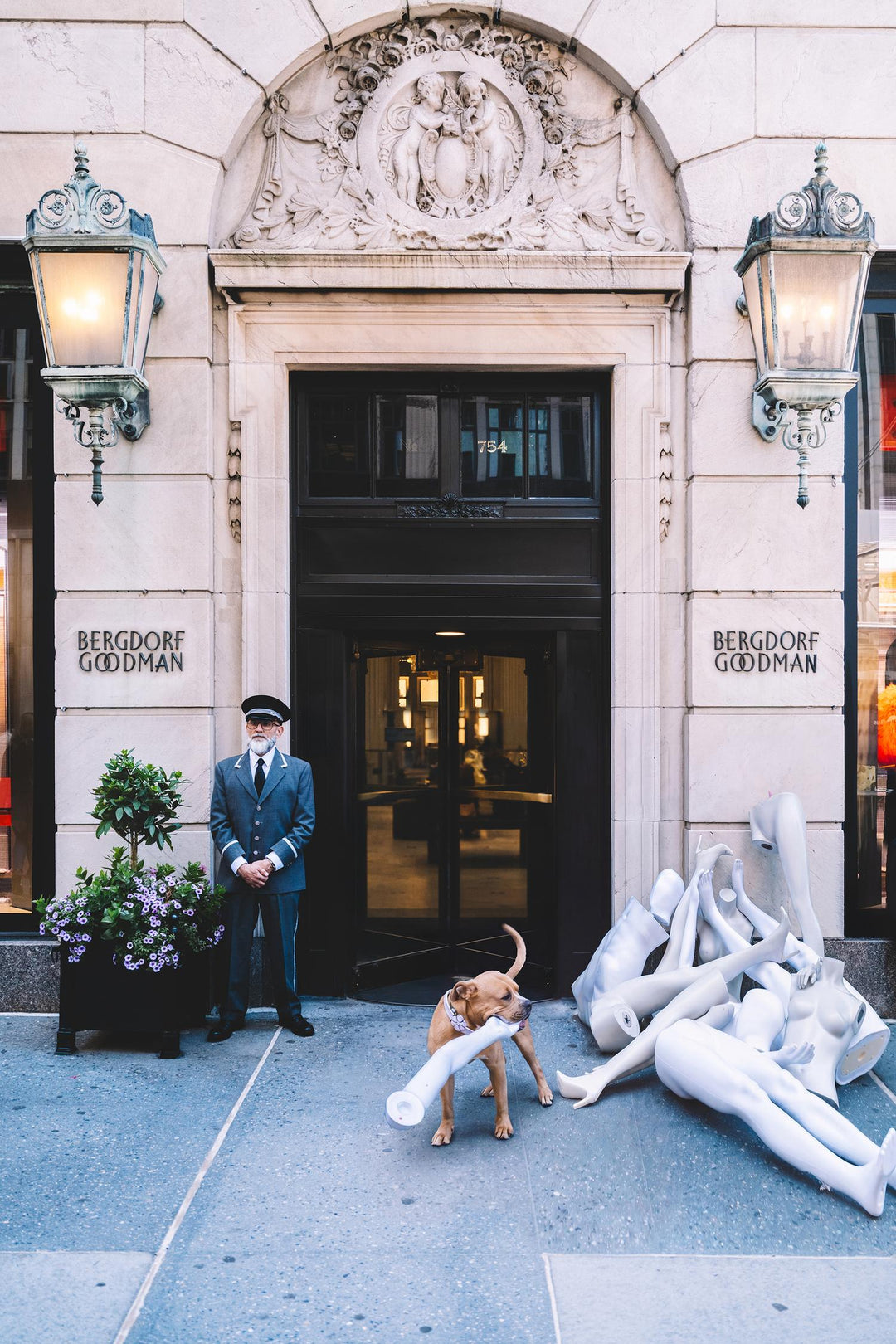 Dog carries a mannequin leg past a pile of mannequins as a doorman stands at Bergdorf Goodman. Nick Mele x Bergdorf Goodman
