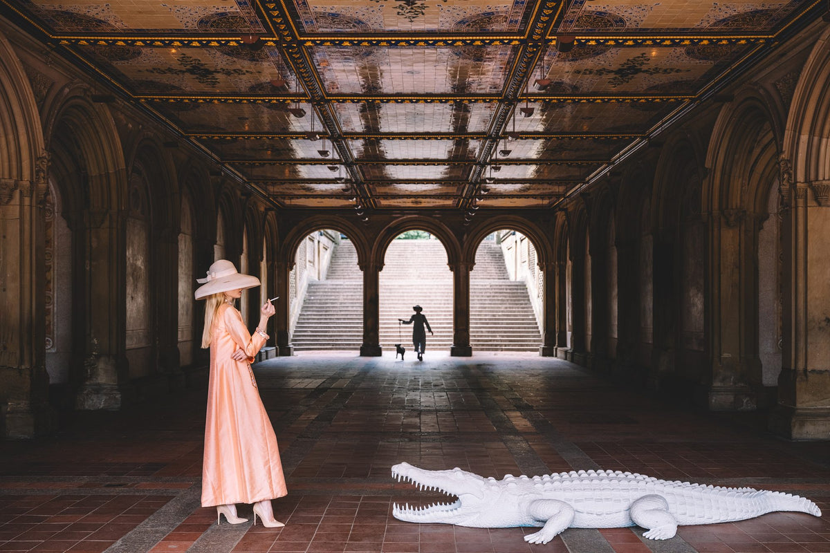 Woman in a peach coat faces a white alligator in Bethesda Terrace arcade, Central Park. Nick Mele x Bergdorf Goodman