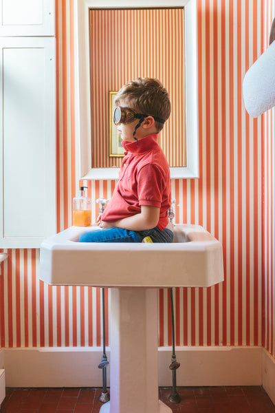 boy in sink with goggles against red and white stripe wallpaper.