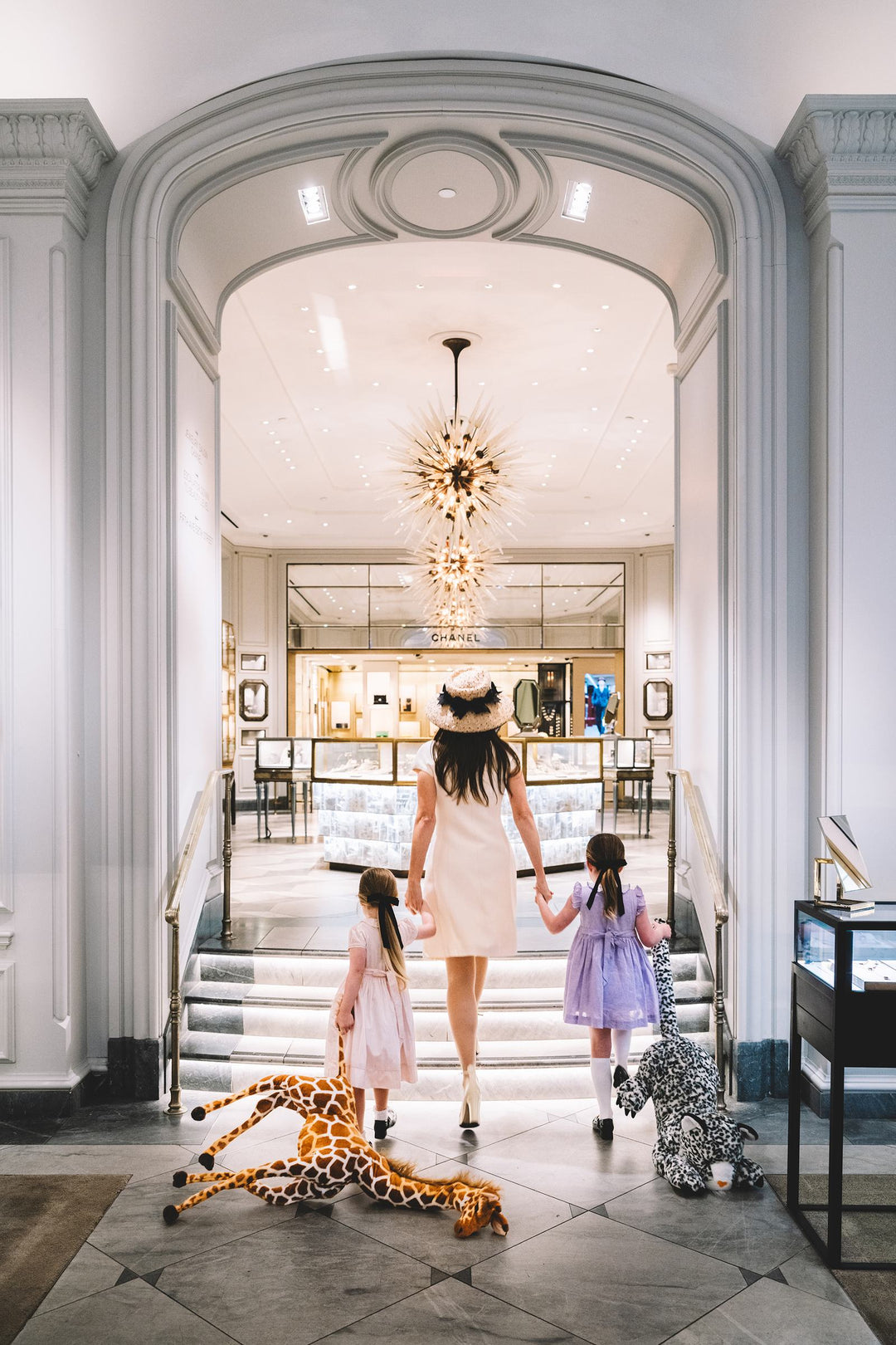 Mother and two daughters walk into the jewelry salon past stuffed animals. Nick Mele x Bergdorf Goodman, A New York Affair