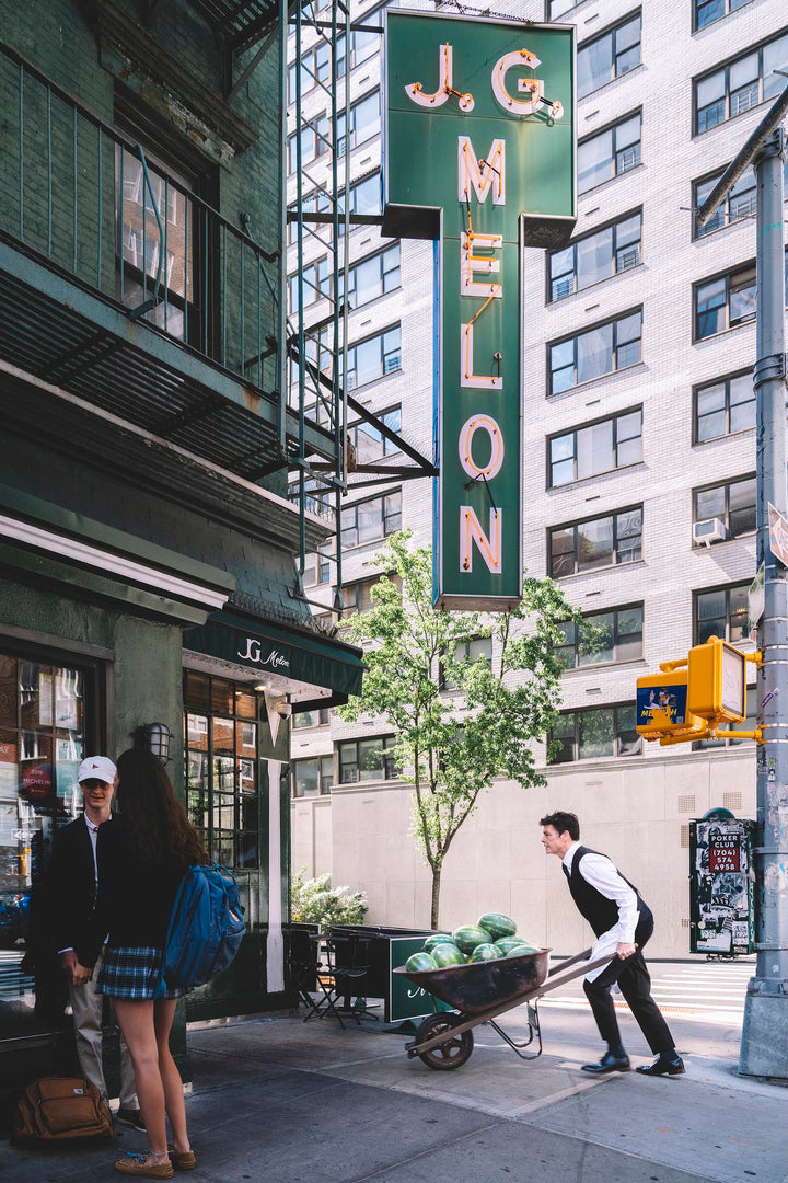 Waiter wheels a barrow of watermelons beneath the J.G. Melon sign. Nick Mele x Bergdorf Goodman, A New York Affair