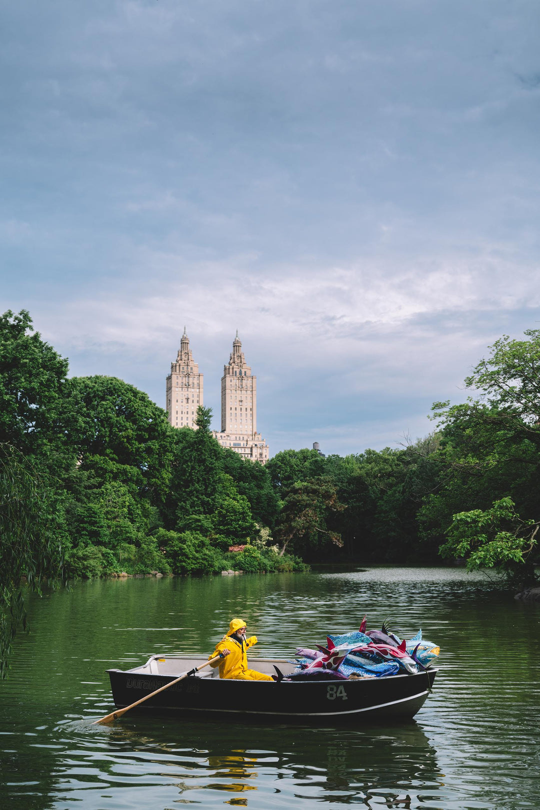 Fisherman in yellow rows a boat of fish on the Central Park Lake below the San Remo. Nick Mele x Bergdorf Goodman