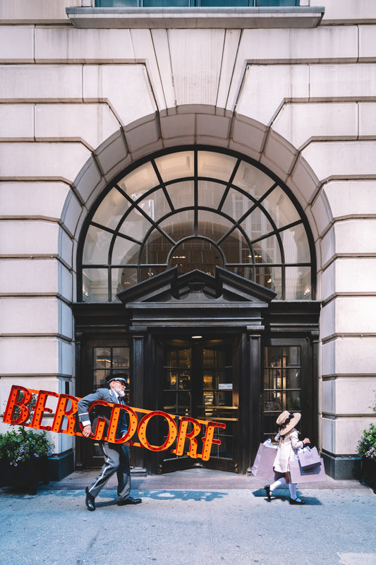 Doorman carries a red marquee Bergdorf sign as a girl follows with shopping bags. Nick Mele x Bergdorf Goodman
